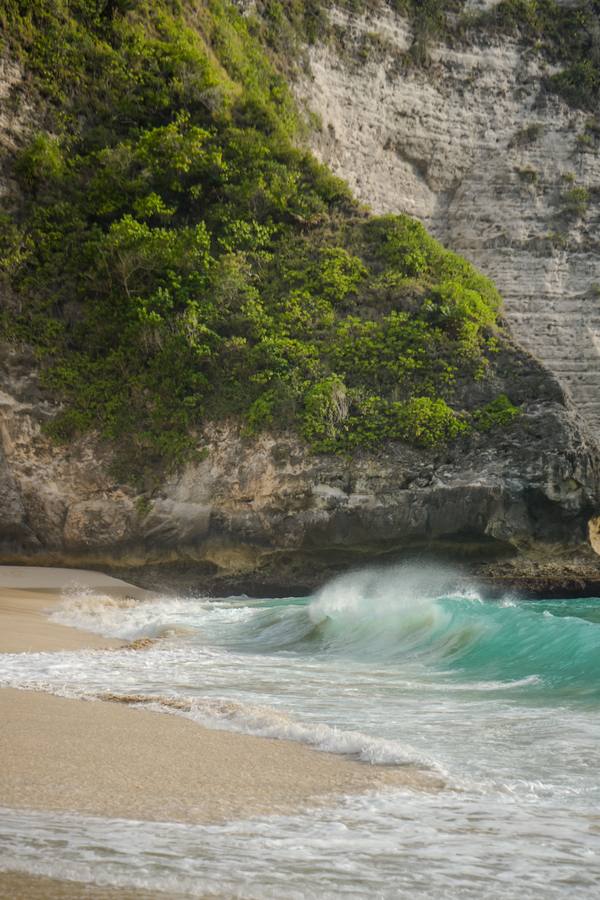Turquoise wave breaking beneath a green cliffside